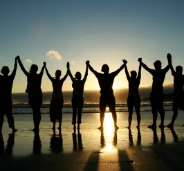 A group of people holding hands on beach as they face the sunset