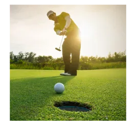 Foreground: golf ball rolling into hole. Background: man in golf attire putting at sunrise. Trees behind him.