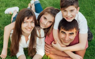 Mom, dad, daughter and son laying on stomachs in grass, hugging and smiling. 