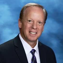 Headshot of Dr. Michael Grego blue background.