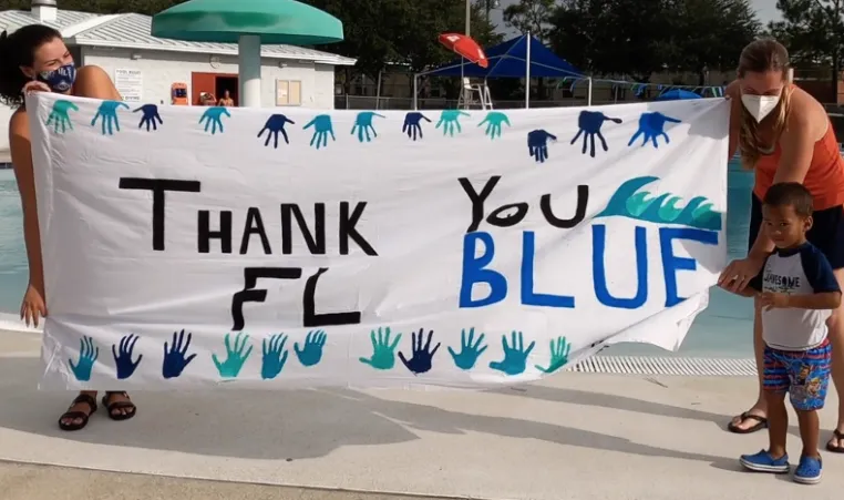 parents holding a handmade banner that says thank you florida blue with young kid