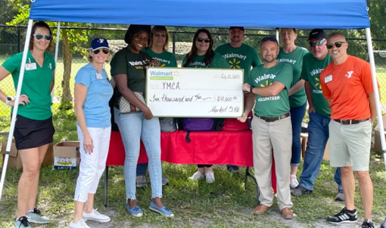 walmart volunteers and YMCA of the Suncoast leaders standing outside under blue tent, smiling and holding check presentation for $10,000 donation