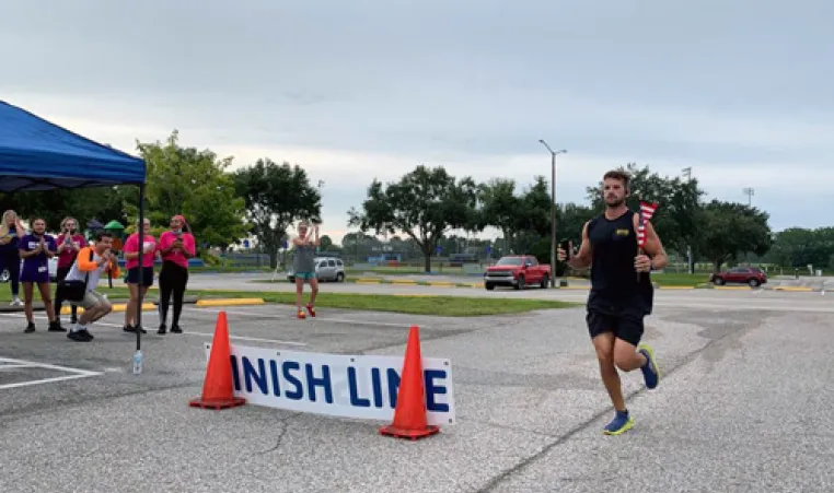 man runs past orange cones and finish line at Run to Remember 2021 event holding a small American flag