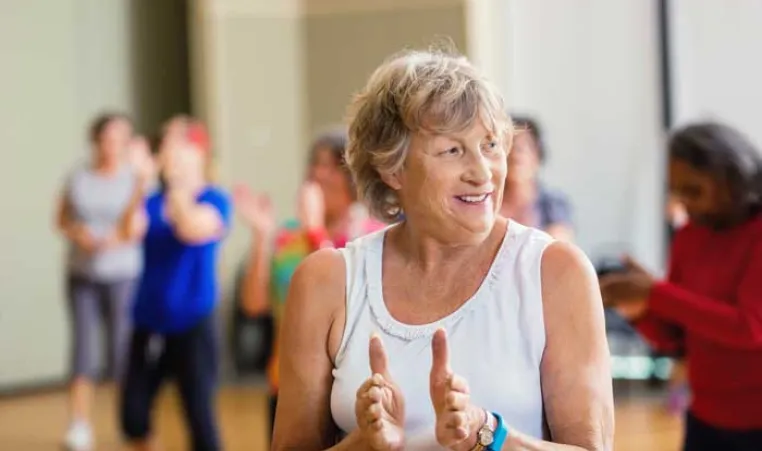 senior woman smiling and clapping in an indoor group exercise class