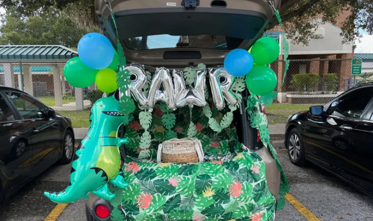 Open car trunk decorated in dinosaur in the jungle theme in a parking lot at a Trunk or Treat event.