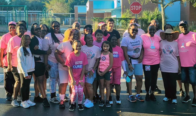 Group of people in a parking lot, wearing pink shirts at a cancer awareness event
