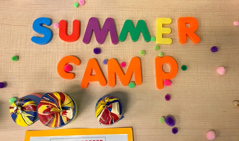 Camp craft call pom pom popper shot from above. Child play letters spell summer camp. Pom poms scattered on the table scene.