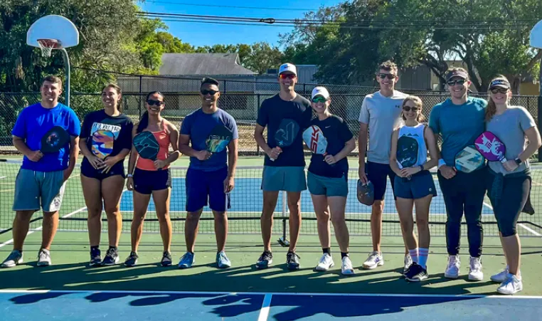 A group of adults standing side by side on an outdoor pickleball court.