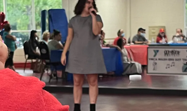 A MASH program participant performing karaoke indoors, in front of friends. The program, MASH, is for adults with physical, cognitive and developmental disabilities, including people who have autism.