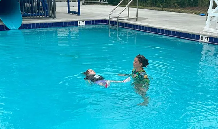 Swim Instructor teaching a young student how to float in the water.