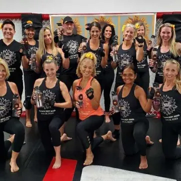 A group of females wearing the same black outfit pose at the end of a group exercise class.
