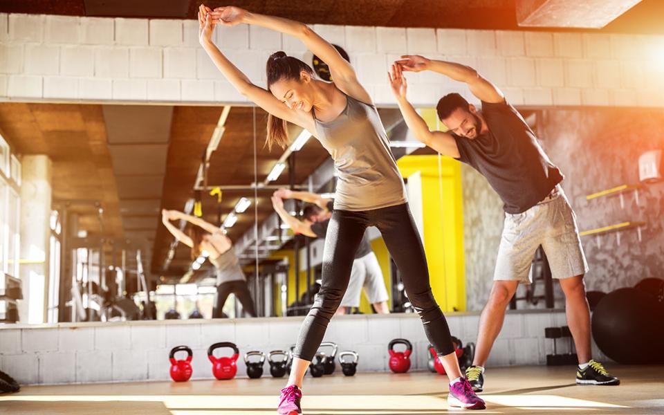 man and woman smiling and stretching in gym