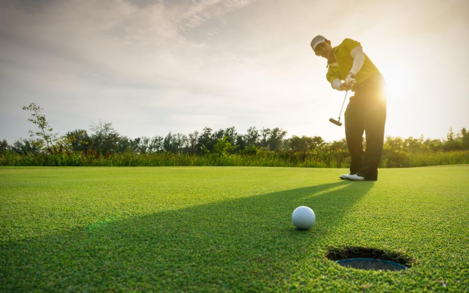 man hitting golf ball with club at sunset